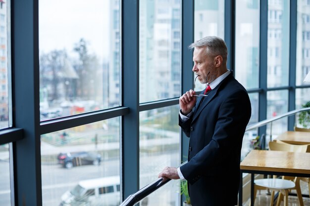 Adult male businessman, teacher, mentor looks out the large window of his office. Work in the office. Development of a new business project