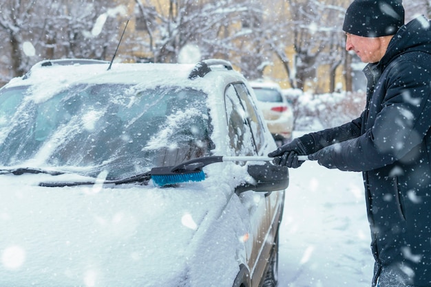 Adult male clean car windshield from snow in blizzard