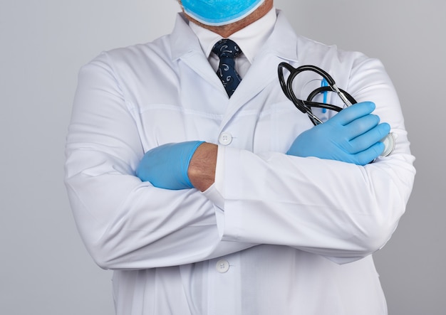 Adult male doctor in a white medical coat stands and holds a black stethoscope