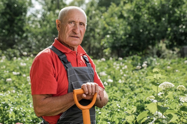 An adult male farmer posing with a shovel in the background of the farm