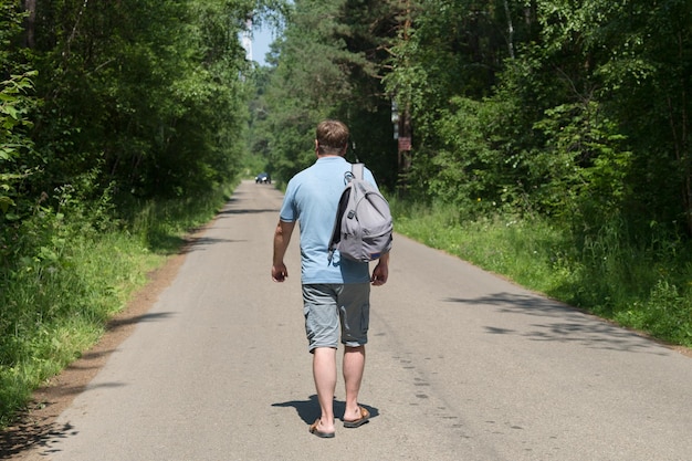 Photo an adult male traveler with a backpack is walking alone on an empty road in the middle of the forest