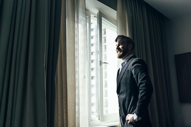 Adult male with a beard in an elegant suit standing near the windows