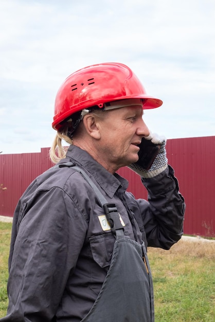 Foto un lavoratore maschio adulto in tuta e un elmetto sta parlando al telefono per strada