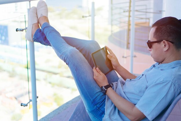 Adult male working on tablet while sitting on the balcony of his home.