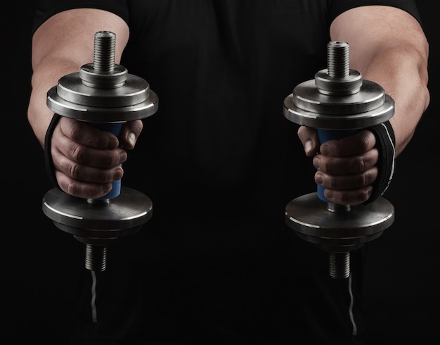 Adult man in black clothes holds steel dumbbells in his hands