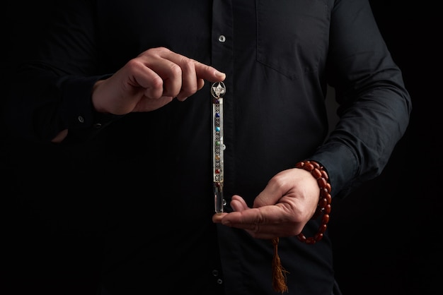 Adult man in a black shirt holds a crystal chakra rod inlaid with semiprecious stones