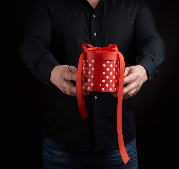 Adult man in a black shirt holds in his hand a round red box of polka dots with a red bow