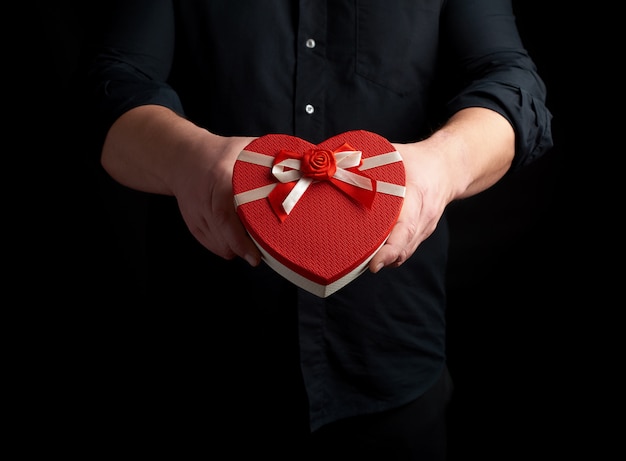 Adult man in a black shirt holds a red cardboard box in the form of a heart with a bow