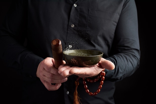 Adult man in a black shirt rotates a wooden stick around a copper Tibetan bowl