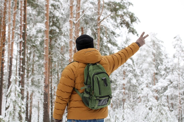 Adult man in casual clothes with a backpack on his back shows a Victory sign