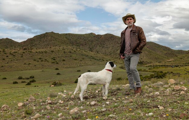 Adult man in cowboy hat and his dog standing on field against sky