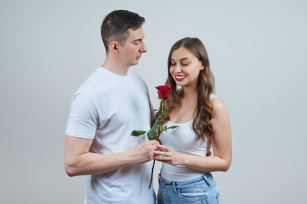 An adult man gives a smiling blonde woman in a white T-shirt a red rose