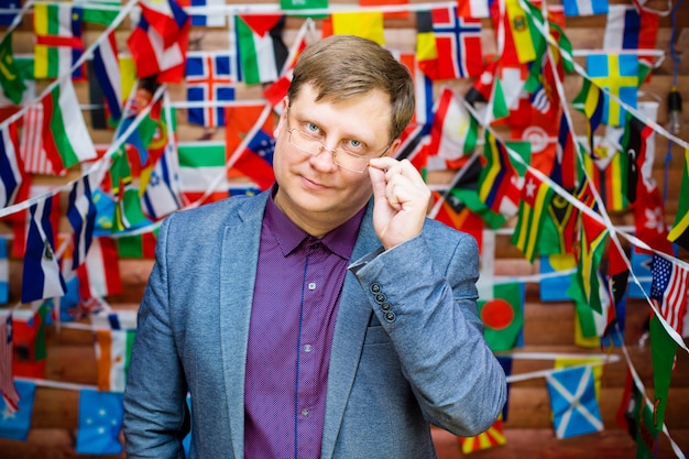 Adult man in glasses against the background of flags of different states.