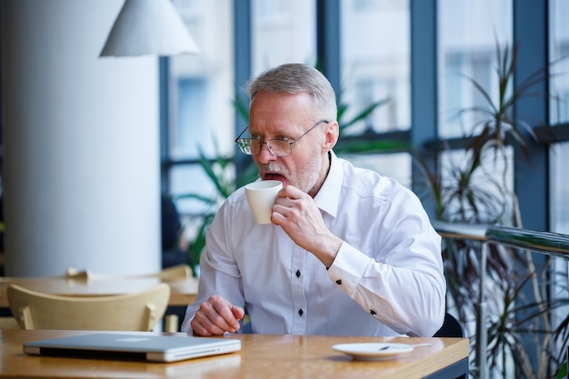 Adult man in glasses manager businessman worked successfully and at the end of the day drinks coffee without a jacket