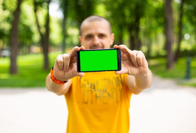 Photo adult man holding cellphone with green chroma key screen standing outdoor in the park