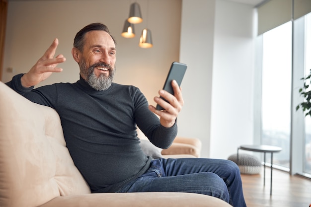 Взрослый мужчина сидит со смартфоном в современной уютной офисной лаунж-зоне