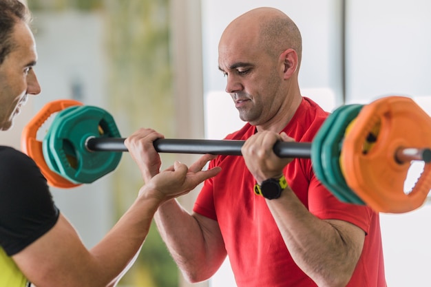 Adult man lifting weights with the help of a personal trainer in a gym