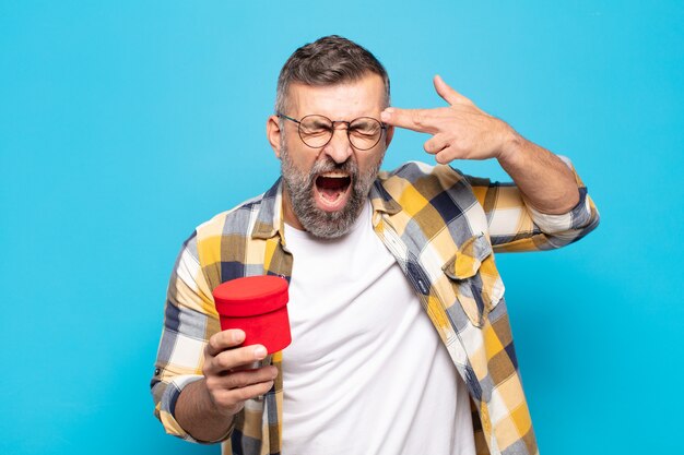 Adult man looking unhappy and stressed, suicide gesture making gun sign with hand, pointing to head