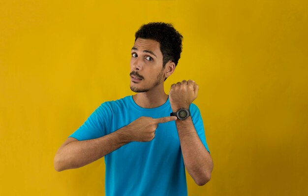 Adult man pointing at his watch on his wrist. Handsome Black Man with blue shirt on yellow.
