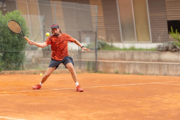 야외 코트에서 테니스를 치는 빨간 티셔츠를 입은 성인 남자