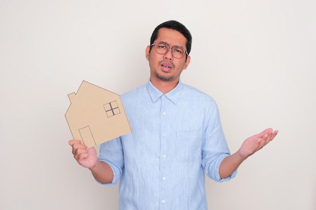 Adult man showing sad expression while holding house shape cardboard