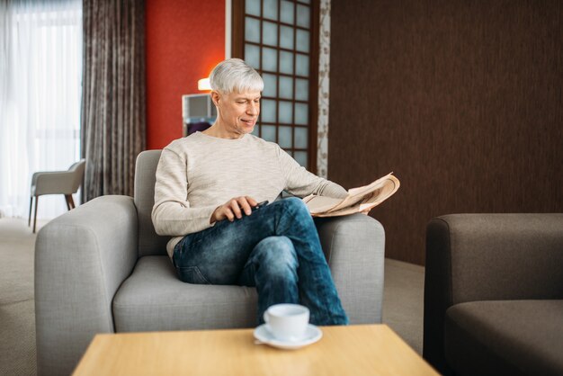 Adult man sitting on couch and reading newspaper