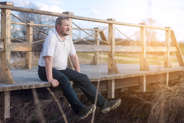 Взрослый мужчина сидит на краю моста летом на улице Взрослый мужчина сидит на краю моста летом на улице