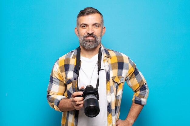 Adult man smiling happily with a hand on hip and confident, positive, proud and friendly attitude