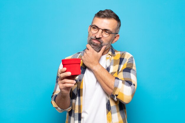 Adult man smiling with a happy, confident expression with hand on chin, wondering and looking to the side