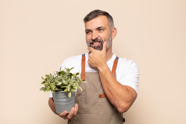 Uomo adulto che sorride con un'espressione felice e sicura con la mano sul mento, chiedendosi e guardando di lato