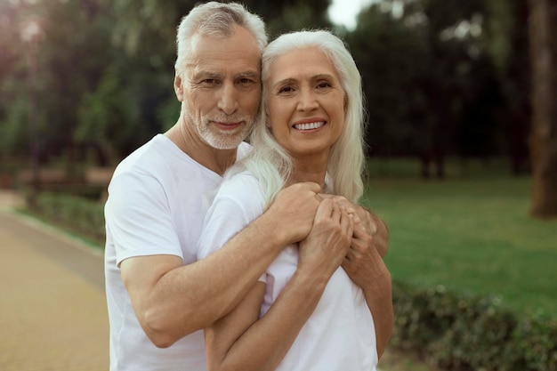 Adult man standing outdoors behind the back of his wife and hugging her