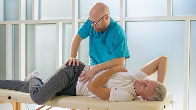 한 성인 남성이 현대 재활 클리닉 병원에서 전문 의사와 함께 근력 운동을 하고 있다.