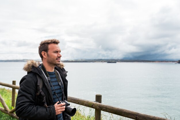 adult man traveler in casual clothes and headband taking photo of rippling sea on camera