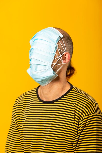 Adult man wearing surgical facial masks covering all his face against a yellow background