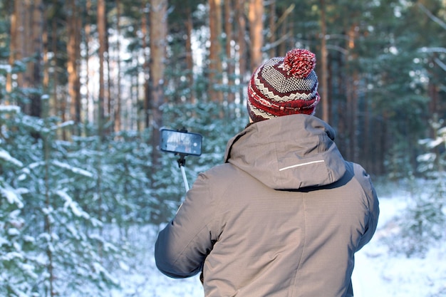 Un uomo adulto in una foresta invernale usa un selfie stick per scattare con uno smartphone persone e tecnologia