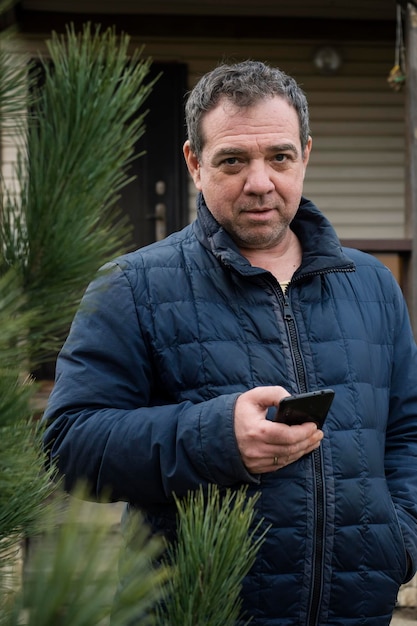 Фото Взрослый мужчина со смартфоном перед своим загородным домом