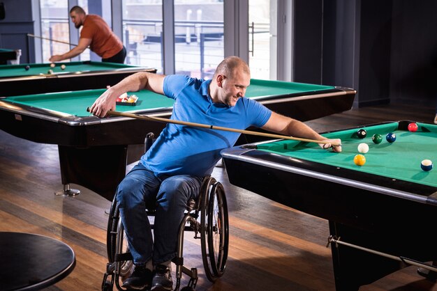 Adult man with disability in a wheelchair play billiards in the club