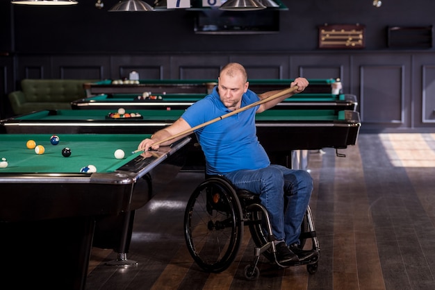 Adult man with disability in a wheelchair play billiards in the club