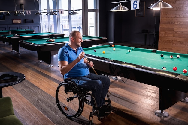 Adult man with disability in a wheelchair play billiards in the club