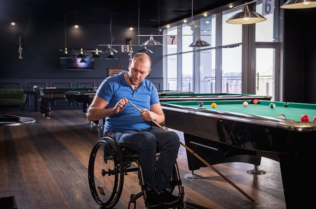 Взрослый человек с ограниченными возможностями в инвалидной коляске играет в бильярд в клубе