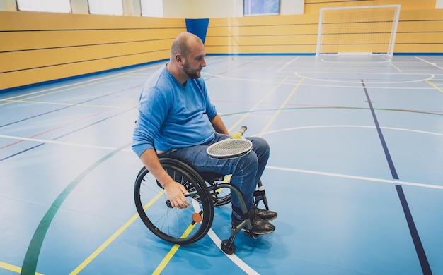 Foto uomo adulto con disabilità fisica su sedia a rotelle che gioca a tennis su un campo da tennis al coperto