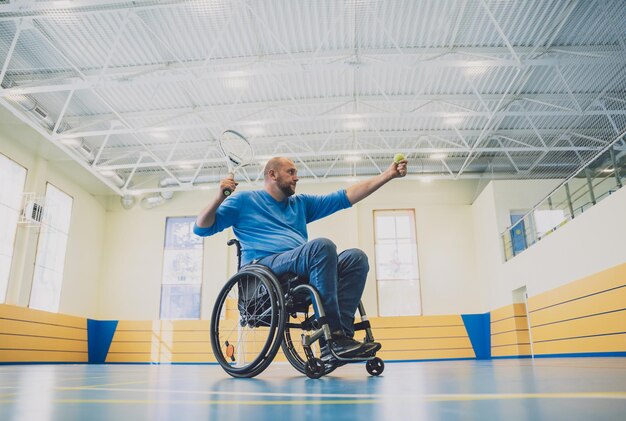 Foto uomo adulto con disabilità fisica su sedia a rotelle che gioca a tennis su un campo da tennis al coperto