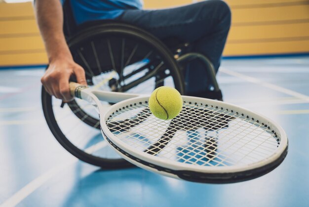 Uomo adulto con disabilità fisica su sedia a rotelle che gioca a tennis su un campo da tennis al coperto