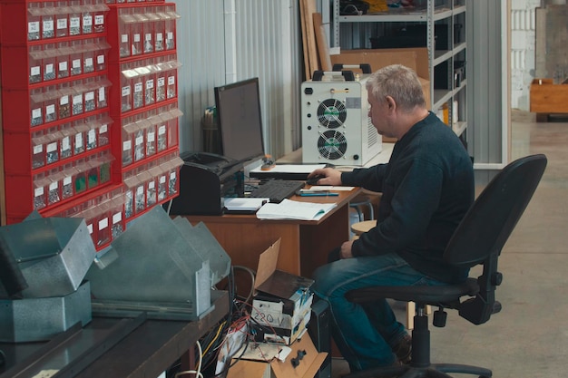 Adult man working at the computer at factory of production CNC machine with lathes, close up