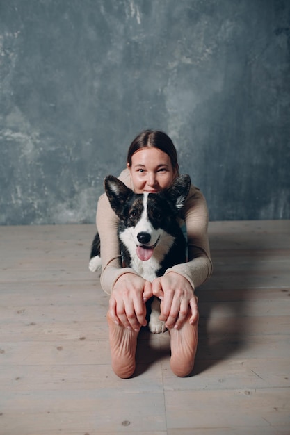 Adult mature woman doing yoga at home in living room with corgi\
dog pet