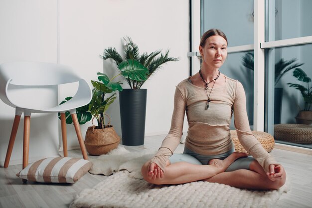 Adult mature woman doing yoga at home living room with online tutorials on laptop