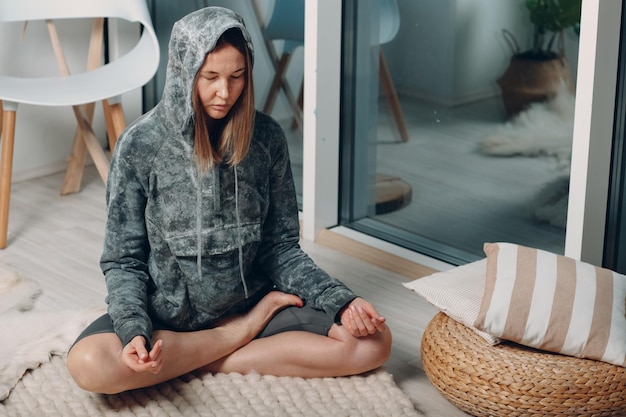 Adult mature woman doing yoga lotus asana at home living room with online tutorials on laptop