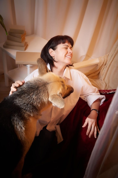 Adult mature woman with big shepherd dog in white shirt room with girl and calm cozy evening