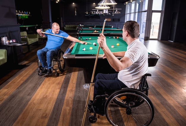 Adult men with disabilities in a wheelchair play billiards in the club