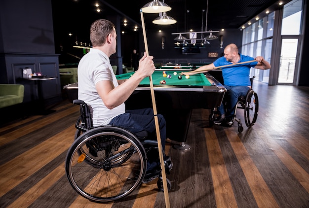 Adult men with disabilities in a wheelchair play billiards in the club